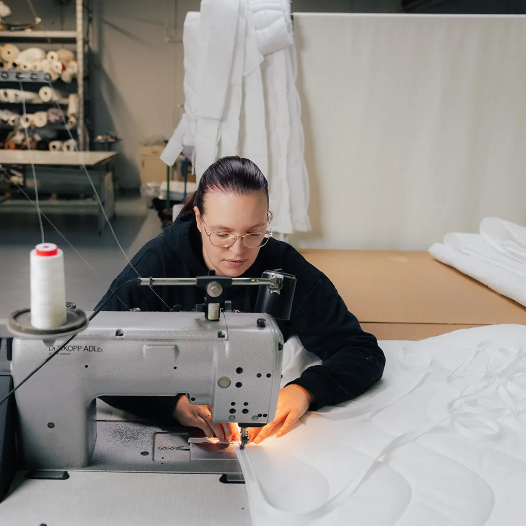 Näherin an der Nähmaschine beim Nähen eines Matratzenbezugs, Nähmaschine, Näherin, Stoff, Weißer Stoff, Produktionswerkstatt